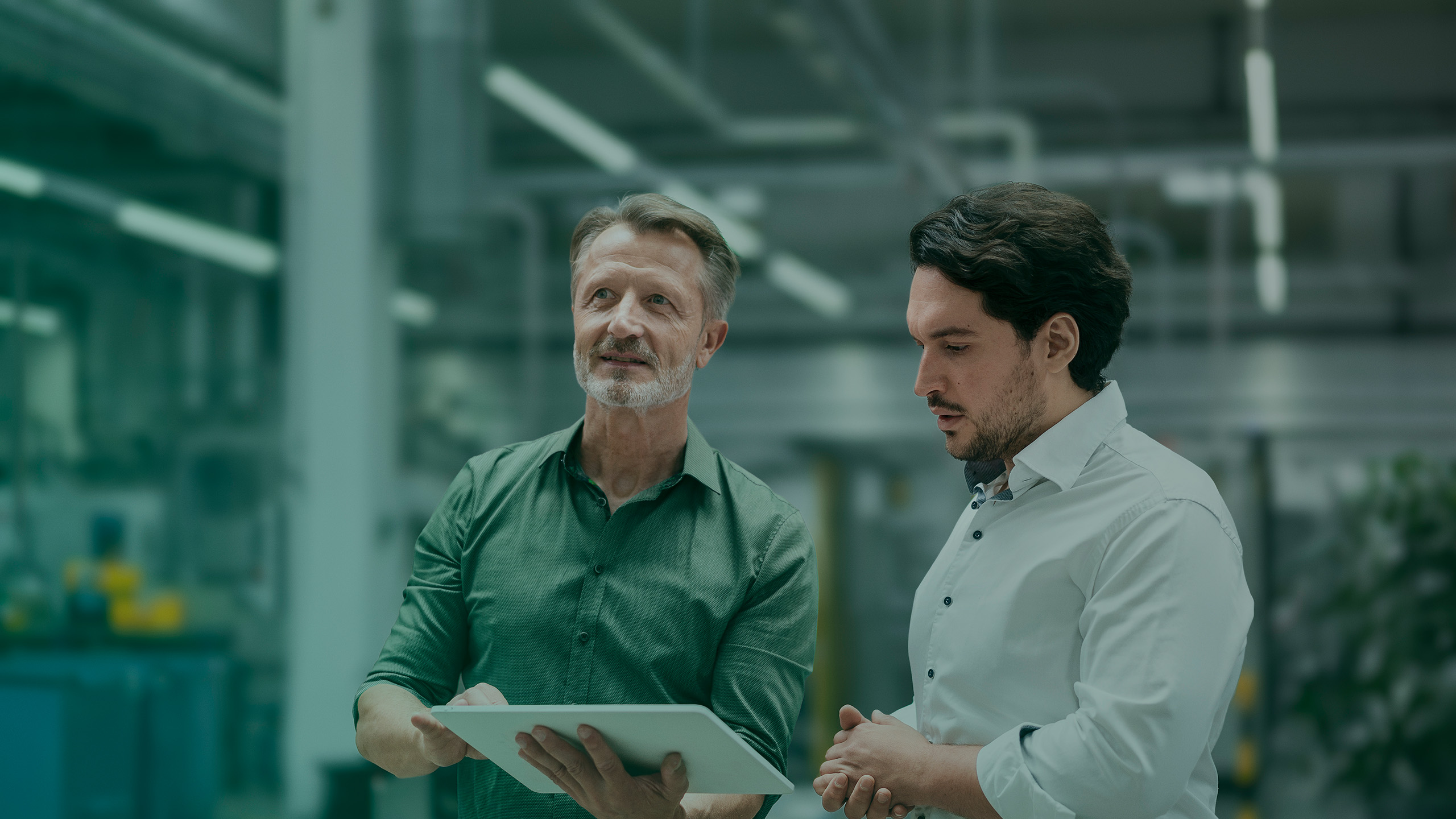 Two colleagues in a modern factory looking at a tablet.