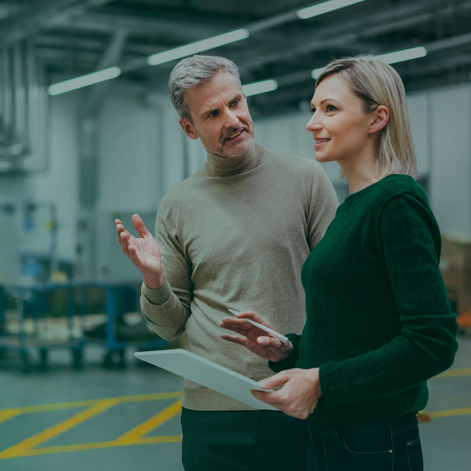 Businessman and businesswoman with digital tablet talking in factory.